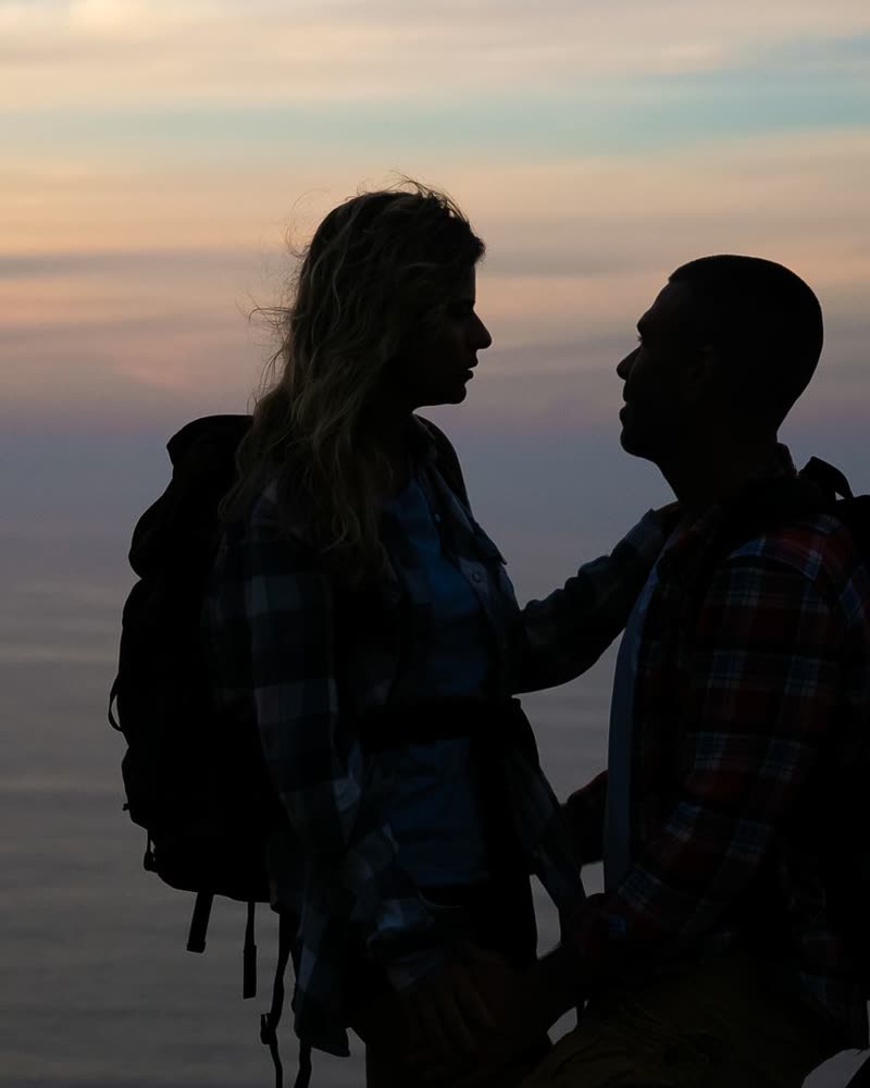 Pareja con mochilas mirando el mar al atardecer
